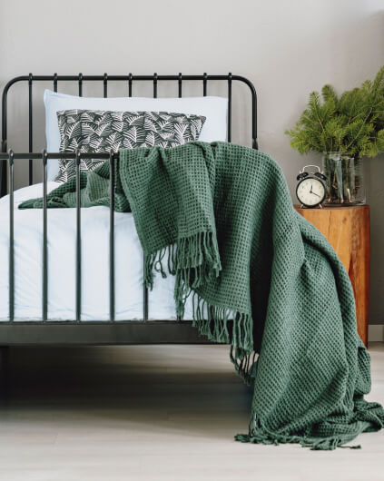 kintoart cozy bed adorned with a green blanket with a stylish clock placed nearby