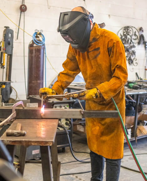 kintoart man in an orange coat skillfully welding metal pieces together in a workshop setting
